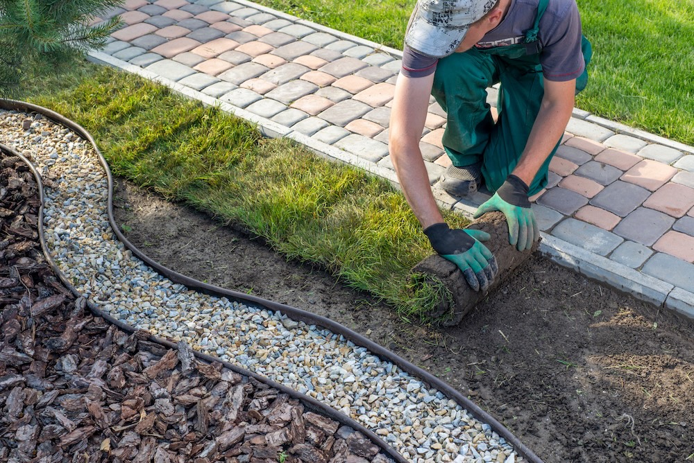 worker laying down sod next to rock pathway