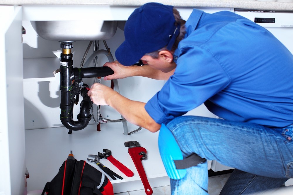 plumber in blue shirt and clothes working on a bathroom sink valve and pipes
